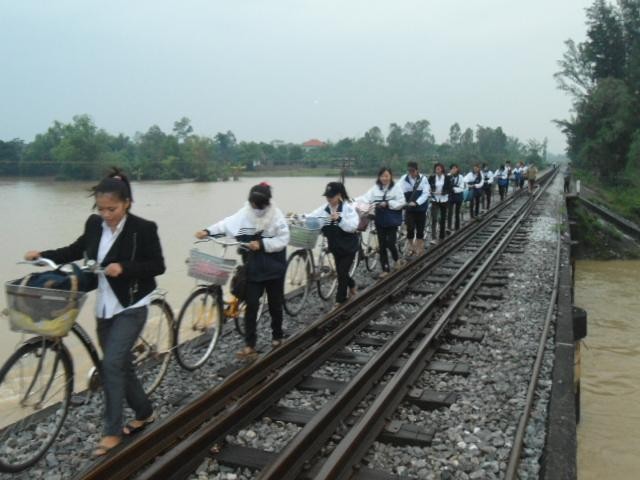 Nhiều em học sinh bám nhau lần lượt men theo đường sắt vượt lũ đến trường trong hiểm nguy